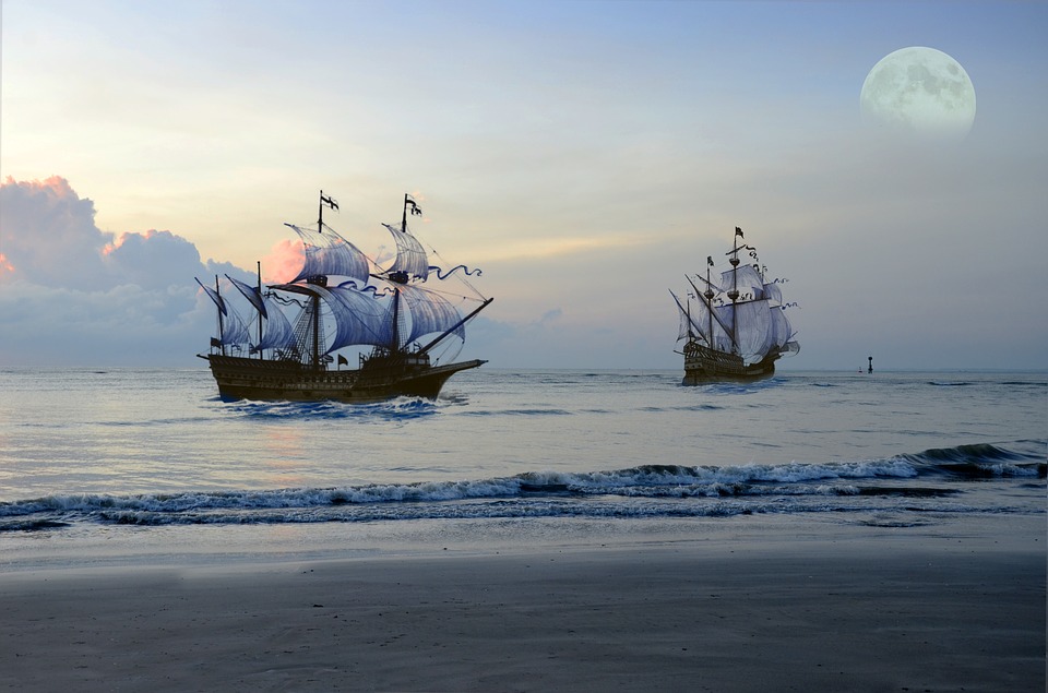 Two historic tall ships sailing at dusk with a full moon rising over calm Caribbean seas