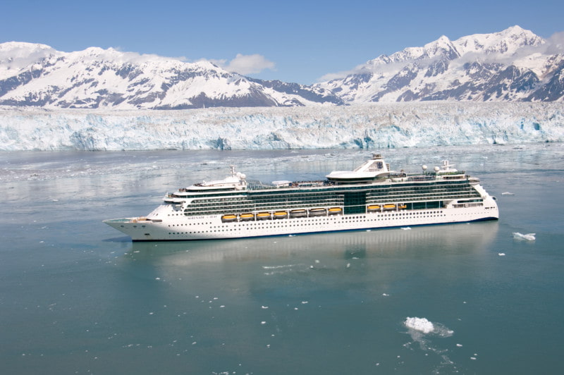 Cruise ship sailing near Hubbard Glacier with snow-capped mountains and floating ice in the surrounding water.
