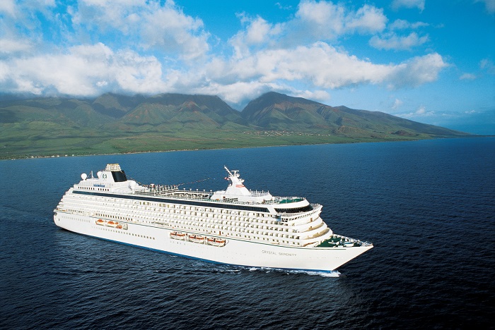 Crystal Serenity luxury cruise ship sailing past volcanic green mountains in Hawaii