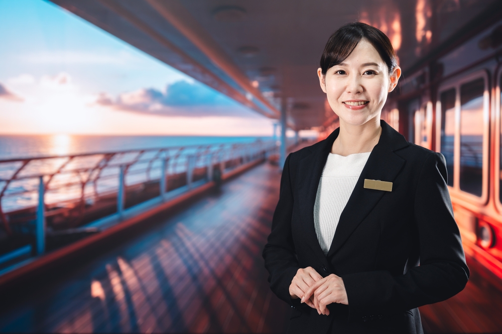 Smiling cruise ship staff member in uniform standing on deck at sunset
