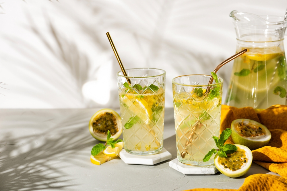 Two passion fruit and lemon cocktails with mint and gold straws on a marble surface