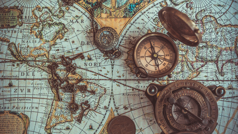 Vintage brass compasses and antique keys laid on an old world navigation map
